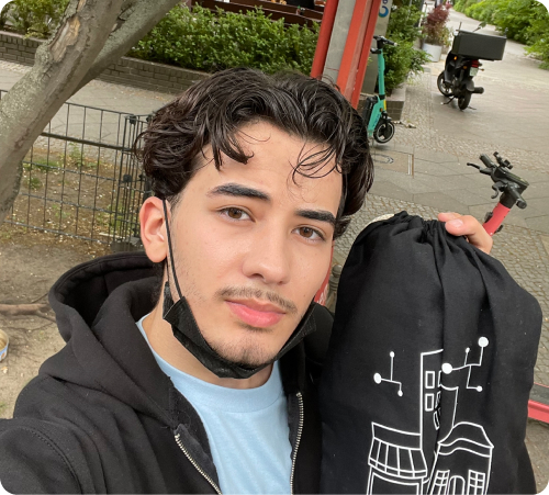 Junger Mann mit einem schwarzen Beutel vor einem E-Scooter