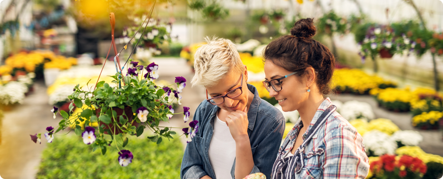 Zwei Frauen mit bunten Pflanzen in einem Gewächshaus