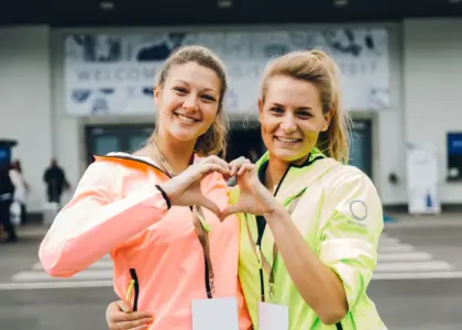 Zwei Frauen auf einer Messe formen ihre Hände gemeinsam zu einem Herzen