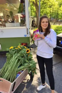 Junge Frau neben einem Bollerwagen gefüllt mit Zeitschriften und Sonnenblumen